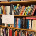 Bilde av bøker i en bokhylle og en lapp der det står posesalg bøker 50 kroner pr pose