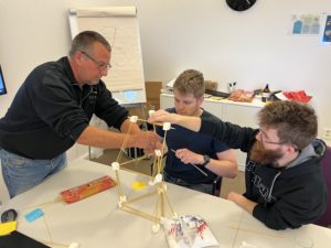 Tre HIM-ansatte som bygger spaghetti- og marshmallowstårn