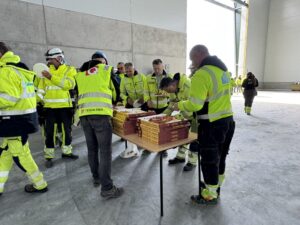 Folk i gule arbeidsklær står i kø for å forsyne seg med pizza