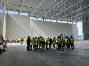 BIlde tatt inne i sorteringshallen, der mange arbeidsfolk i gule synlighetsklær står samlet 